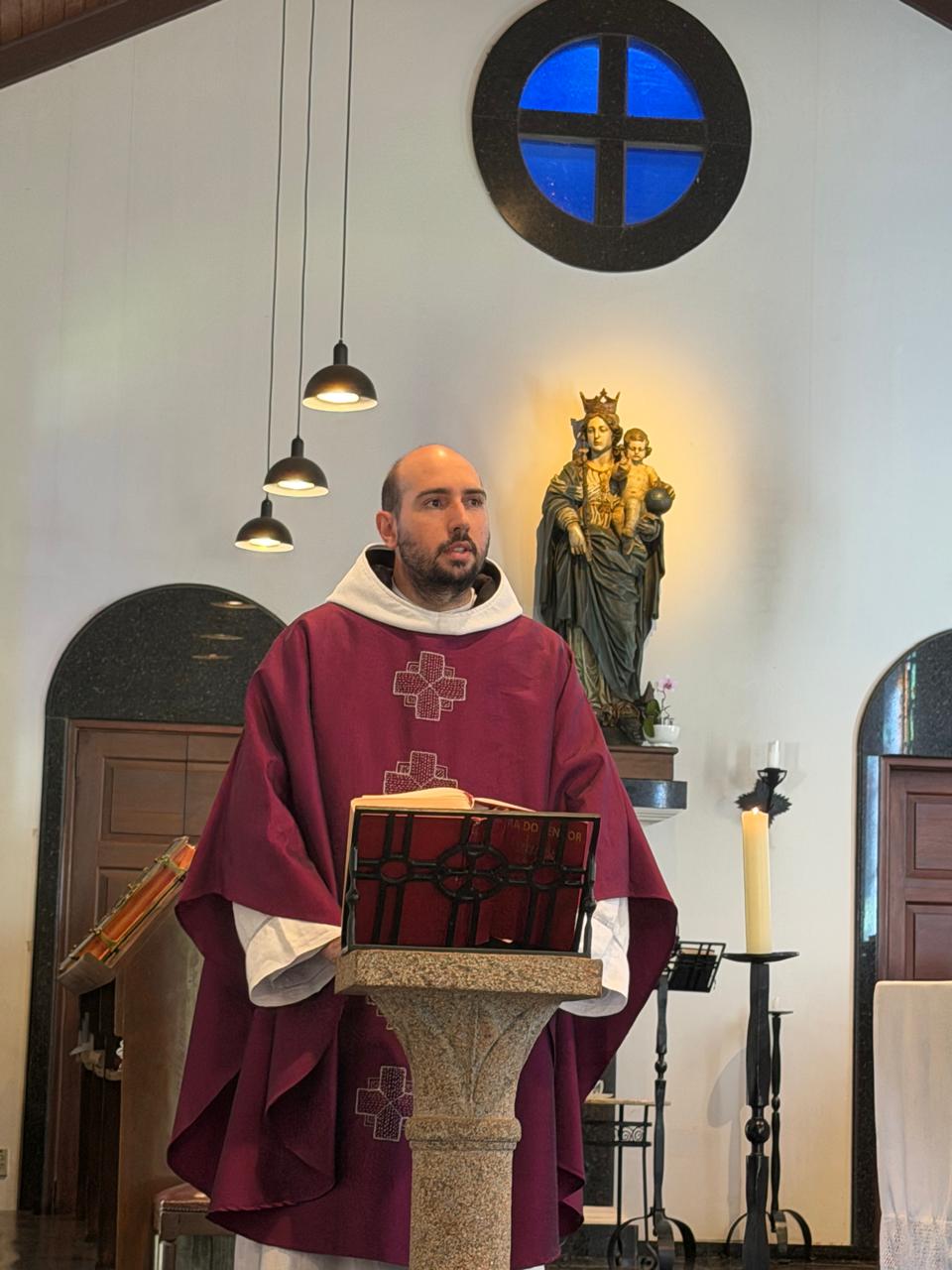 Um monge faz a homilia no ambão, de casula roxa, junto à imagem de Nossa Senhora